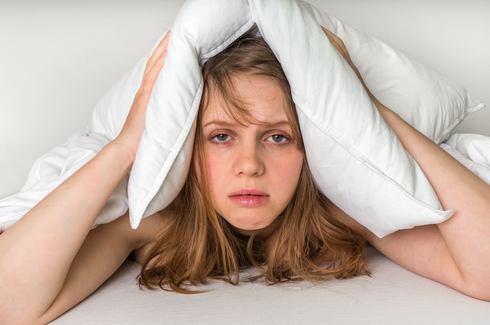 Young,Woman,In,Bed,Covering,Ears,With,Pillow,Because,Of